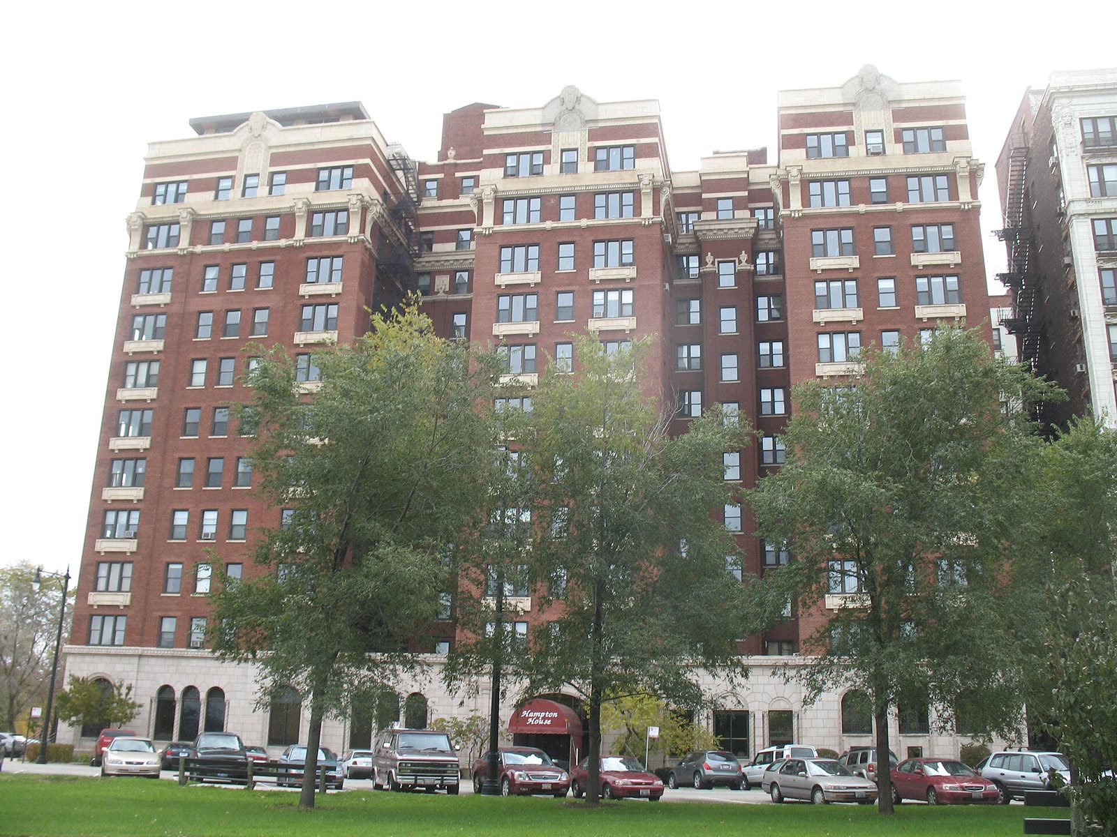 The Hampton House today, a red brick tower with a red entrance awning behind park trees