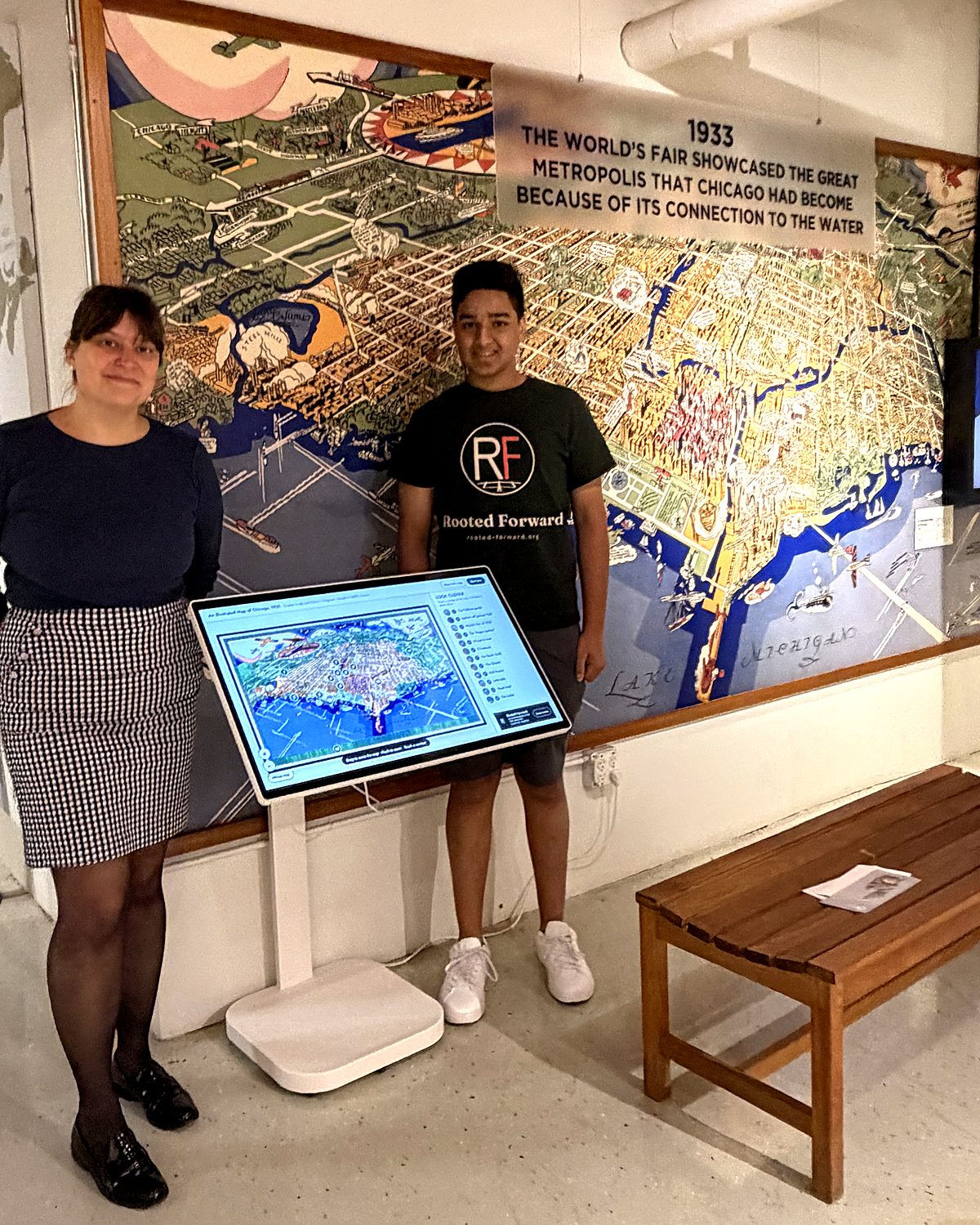 The 1931 map of Chicago mounted on a wall at the Chicago Maritime Museum, with a touch screen showing the interactive guide in front of it and two people standing beside it